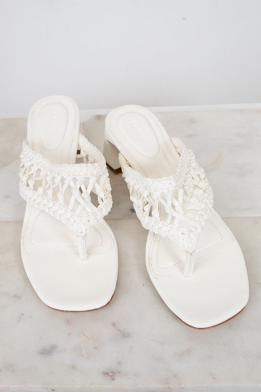 Pair of white sandals with crochet straps on a marble surface