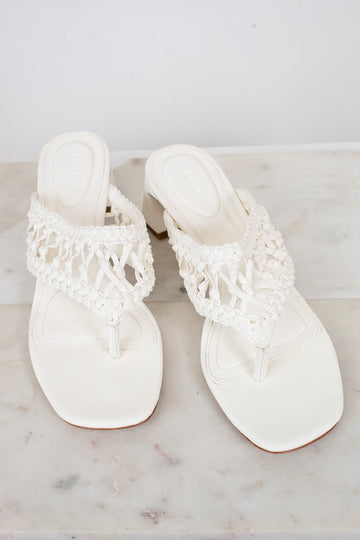 Pair of white sandals with crochet straps on a marble surface