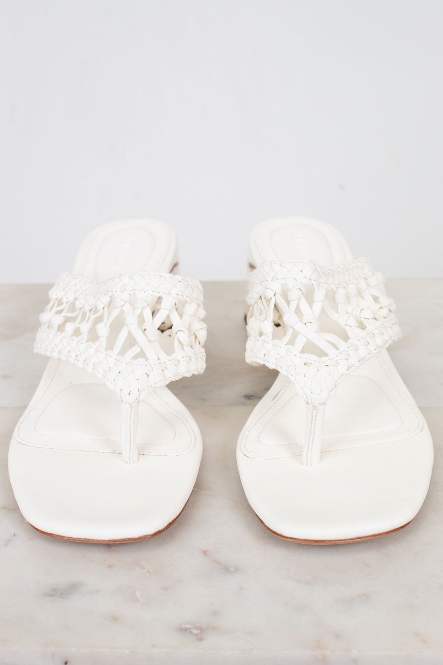 Pair of white sandals with lace details on a marble surface