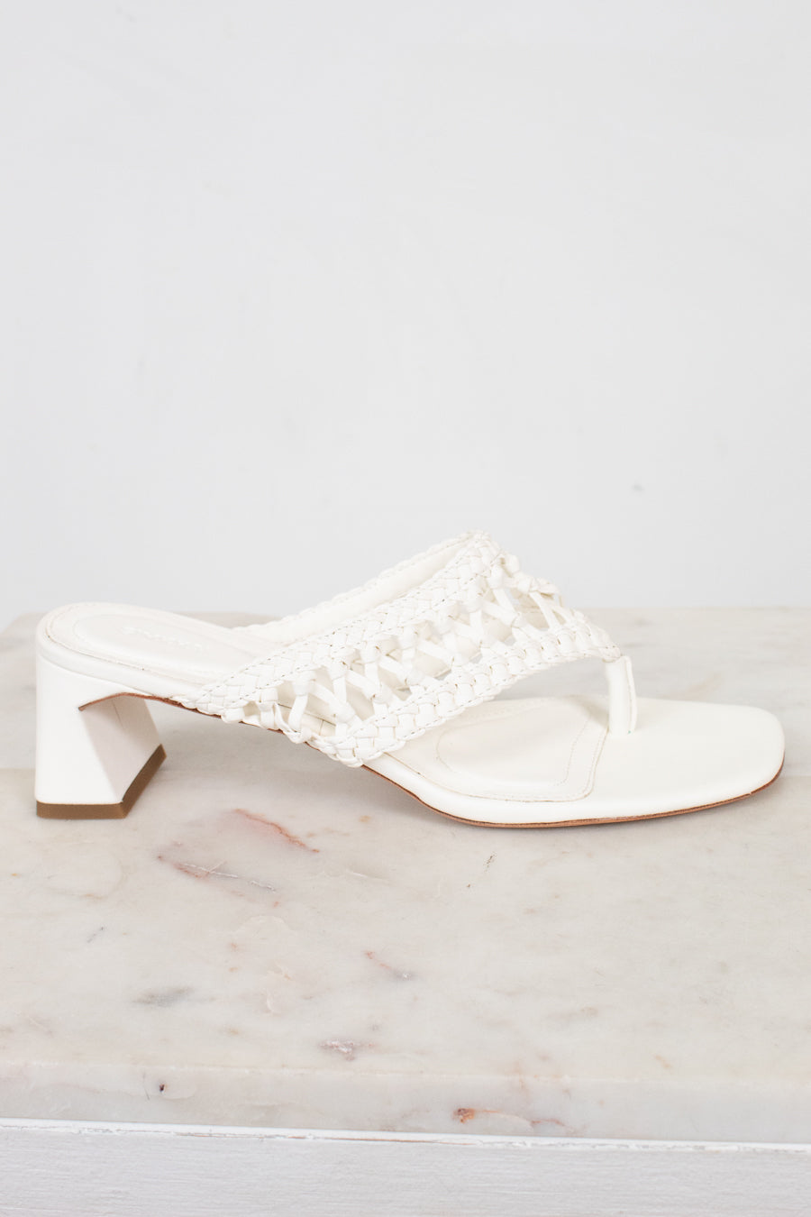 White sandal with crochet like details on a marble surface