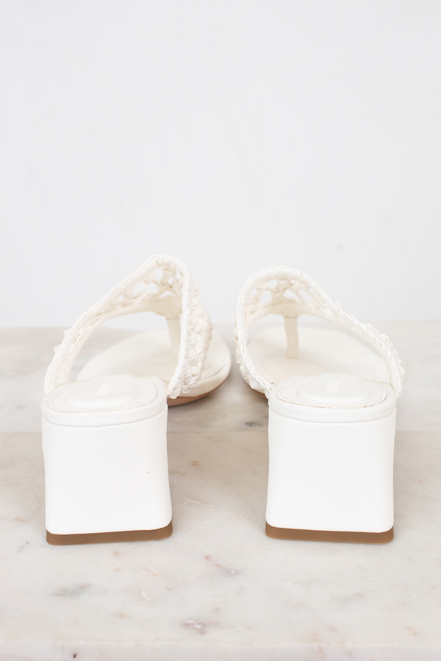 White block heeled sandals on a marble surface
