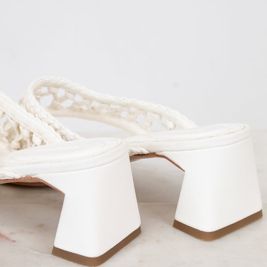 White high-heeled shoes with a textured strap on a light gray background