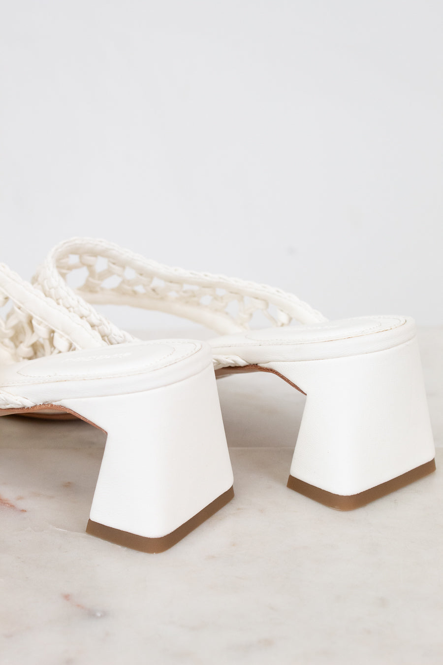 White high-heeled shoes with a textured strap on a light gray background