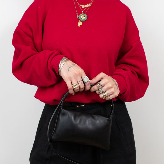 Person wearing a red sweater and black pants holding a black bag against a white background