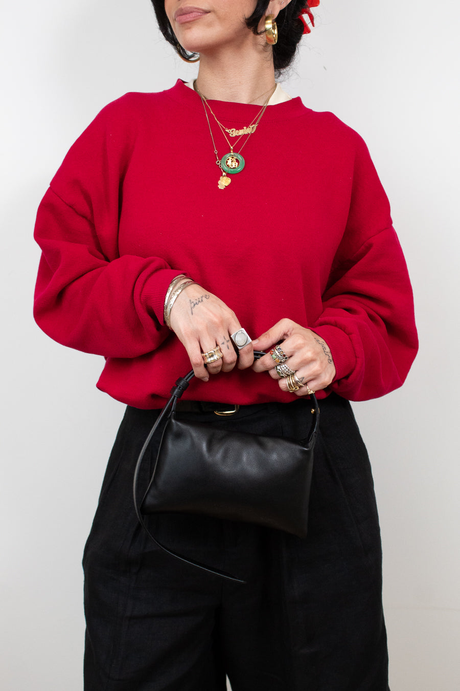 Person wearing a red sweater and black pants holding a black bag against a white background