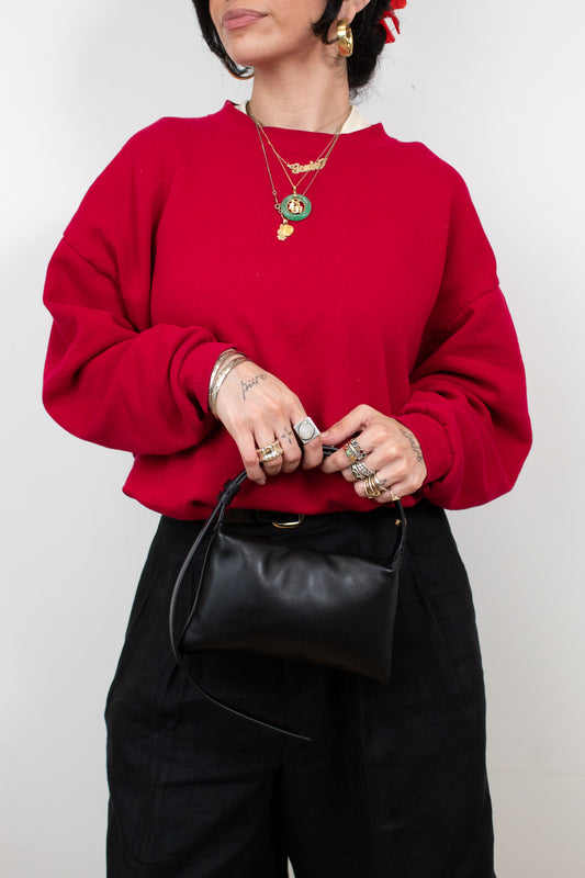 Person wearing a red sweater and black pants holding a black bag against a white background