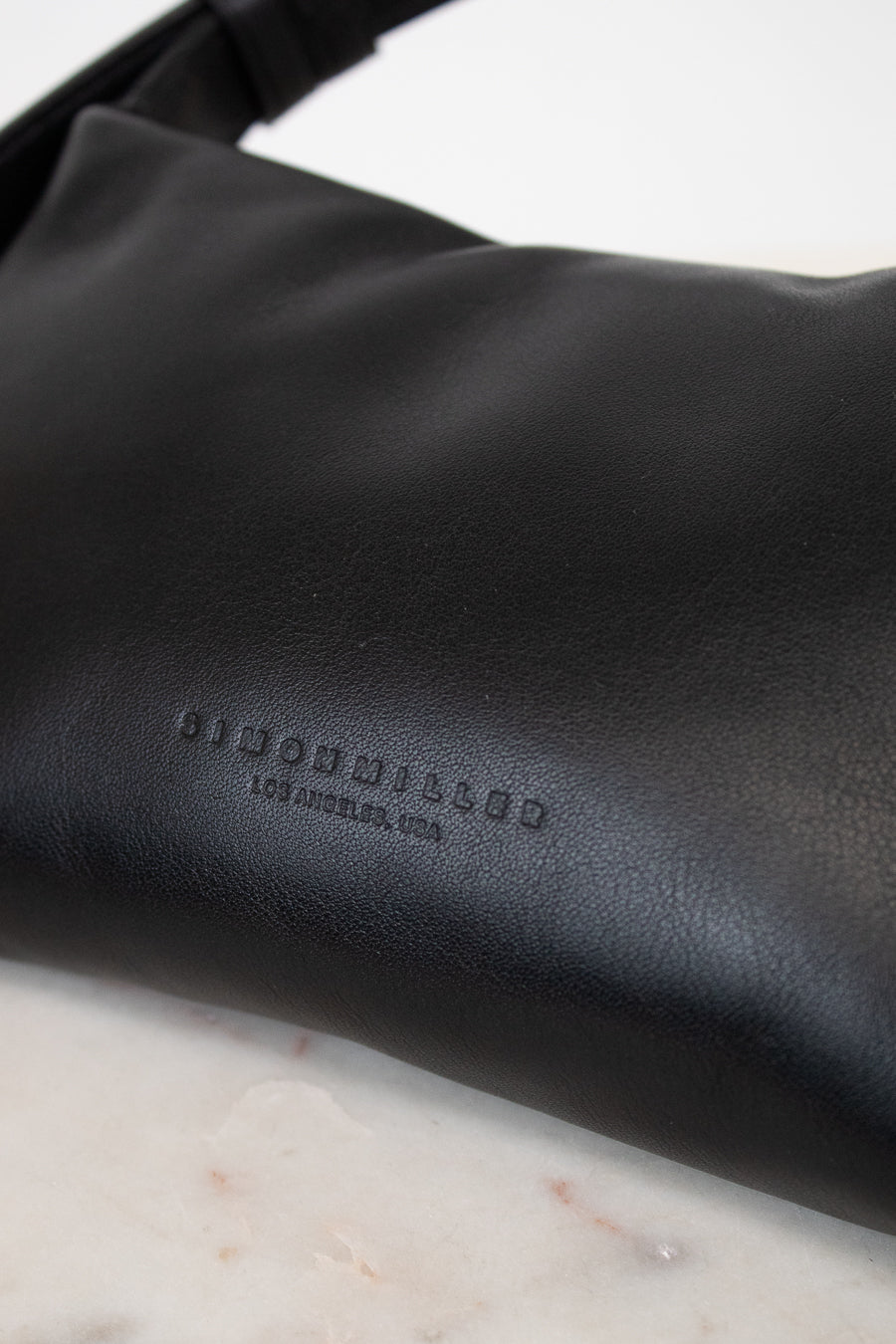 Black leather bag with 'Simon Miller' branding on a marble surface