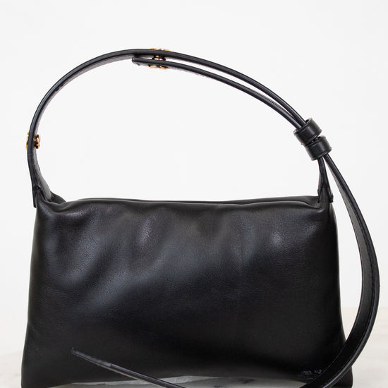 Black leather handbag with a strap on a light gray background