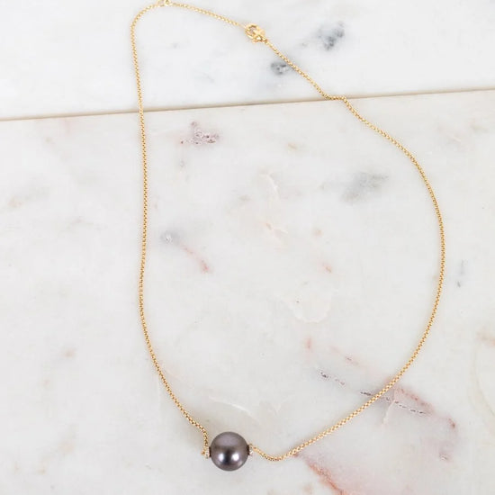 Gold necklace with a single black pearl on a marble surface