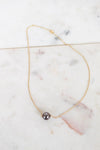 Gold necklace with a single black pearl on a marble surface