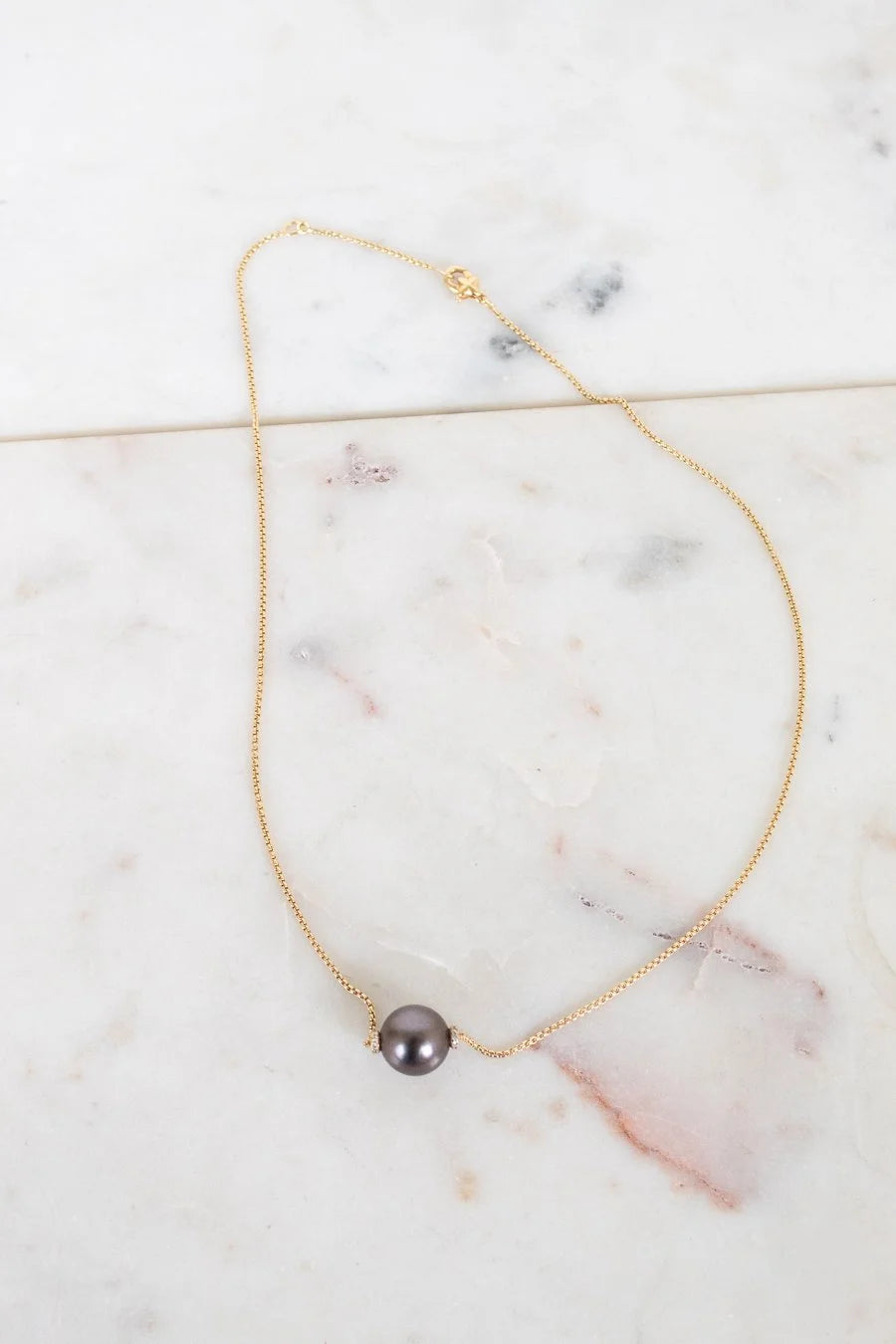 Gold necklace with a single black pearl on a marble surface