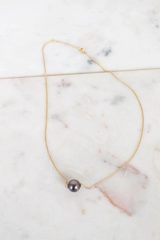 Gold necklace with a single black pearl on a marble surface