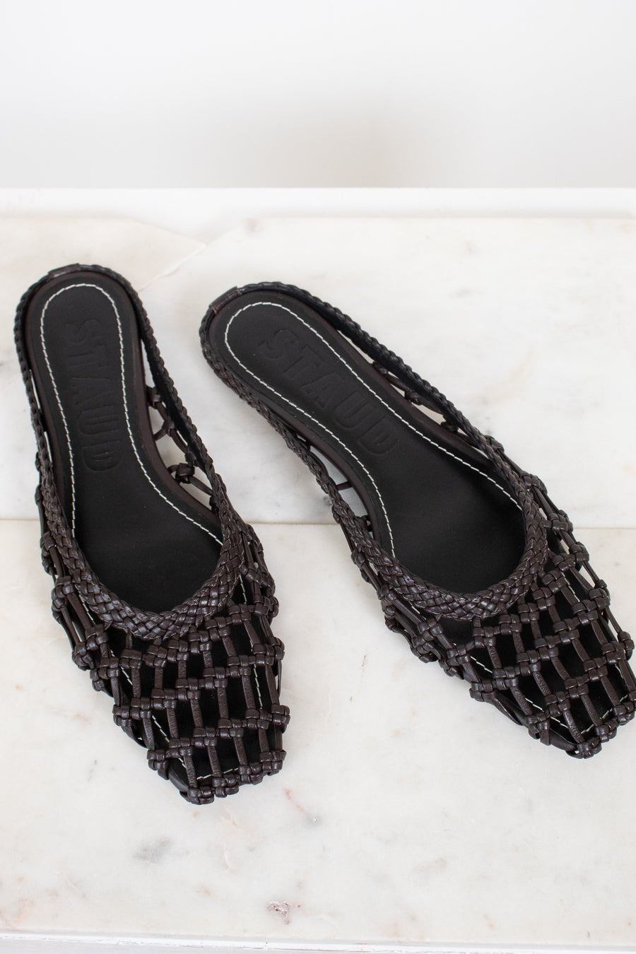 Dark brown woven sandals on a white marble surface