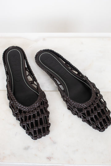 Dark brown woven sandals on a white marble surface