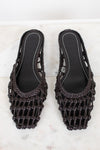Pair of dark brown woven sandals on a light marble background