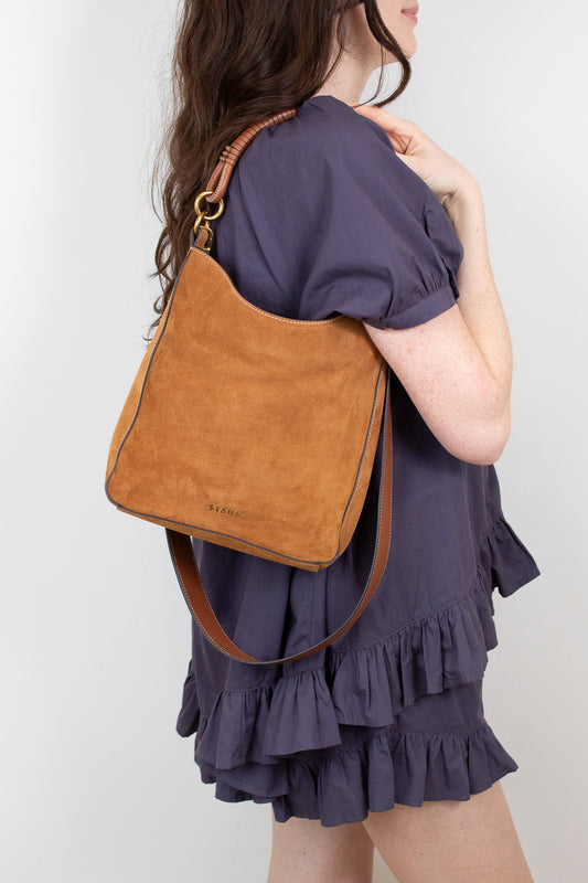 Woman wearing a brown suede and leather shoulder bag on a plain background