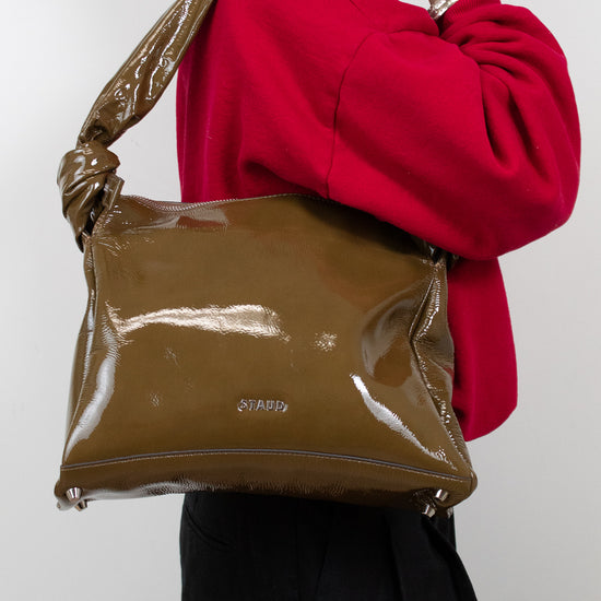 Person wearing a red sweater and holding an olive patent leather handbag against a white background