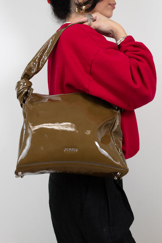 Person wearing a red sweater and holding an olive patent leather handbag against a white background