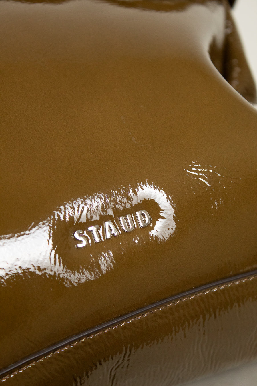 Close-up of an olive leather bag with 'Staud' logo branding.