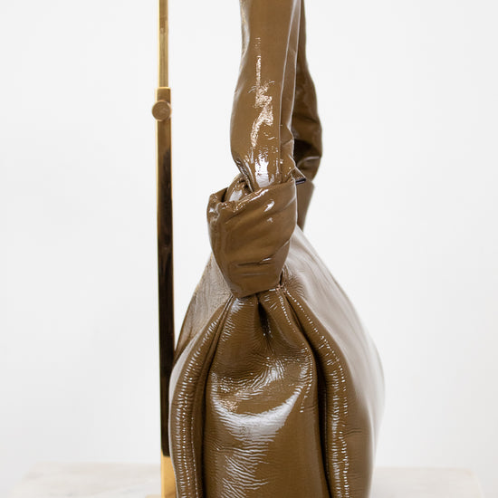 Olive patent leather handbag with a knotted handle detail on a white background