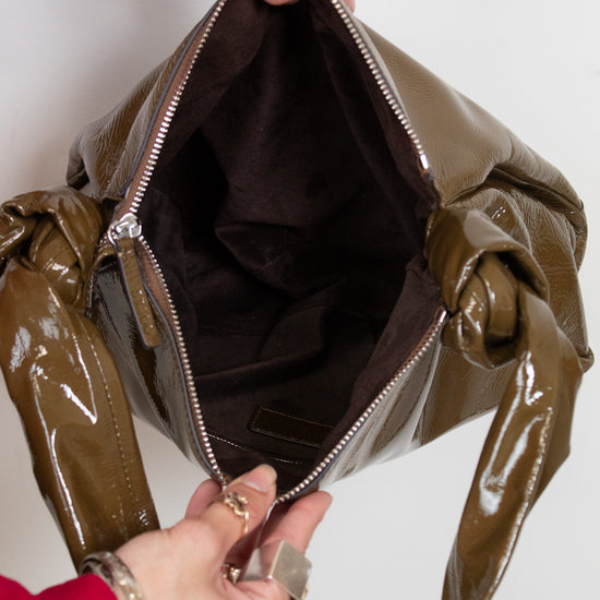 Olive patent leather handbag being held open by a person's hands.