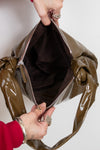 Olive patent leather handbag being held open by a person's hands.