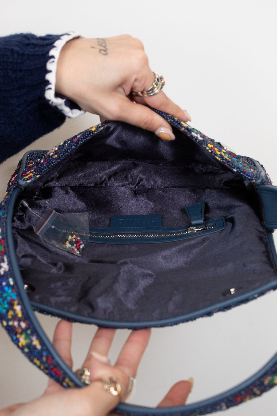 Navy handbag with colorful beaded details held open by a person's hands.