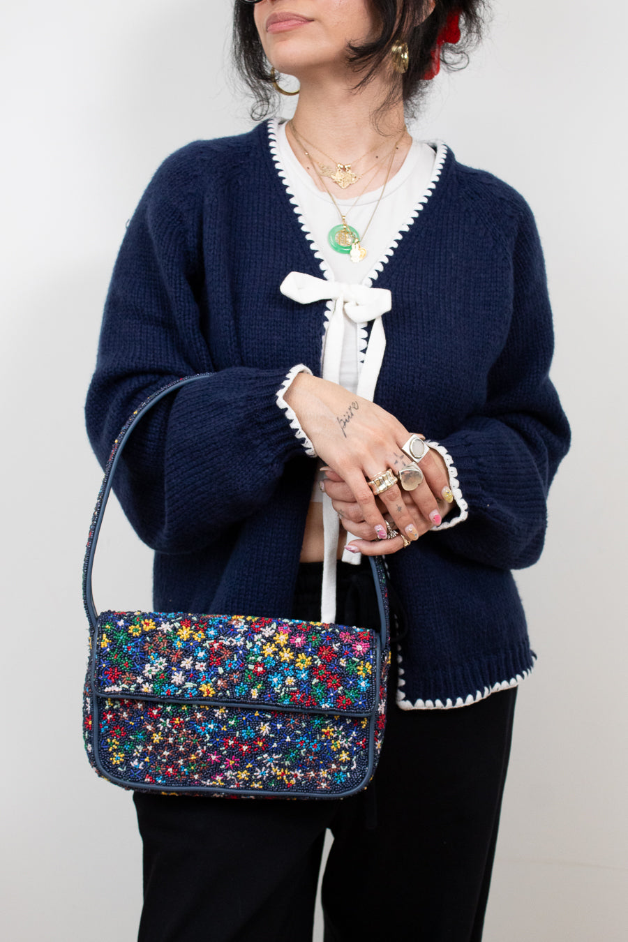Person wearing a navy blue cardigan with a colorful floral beaded handbag.