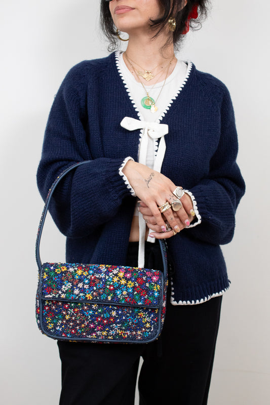 Person wearing a navy blue cardigan with a colorful floral beaded handbag.