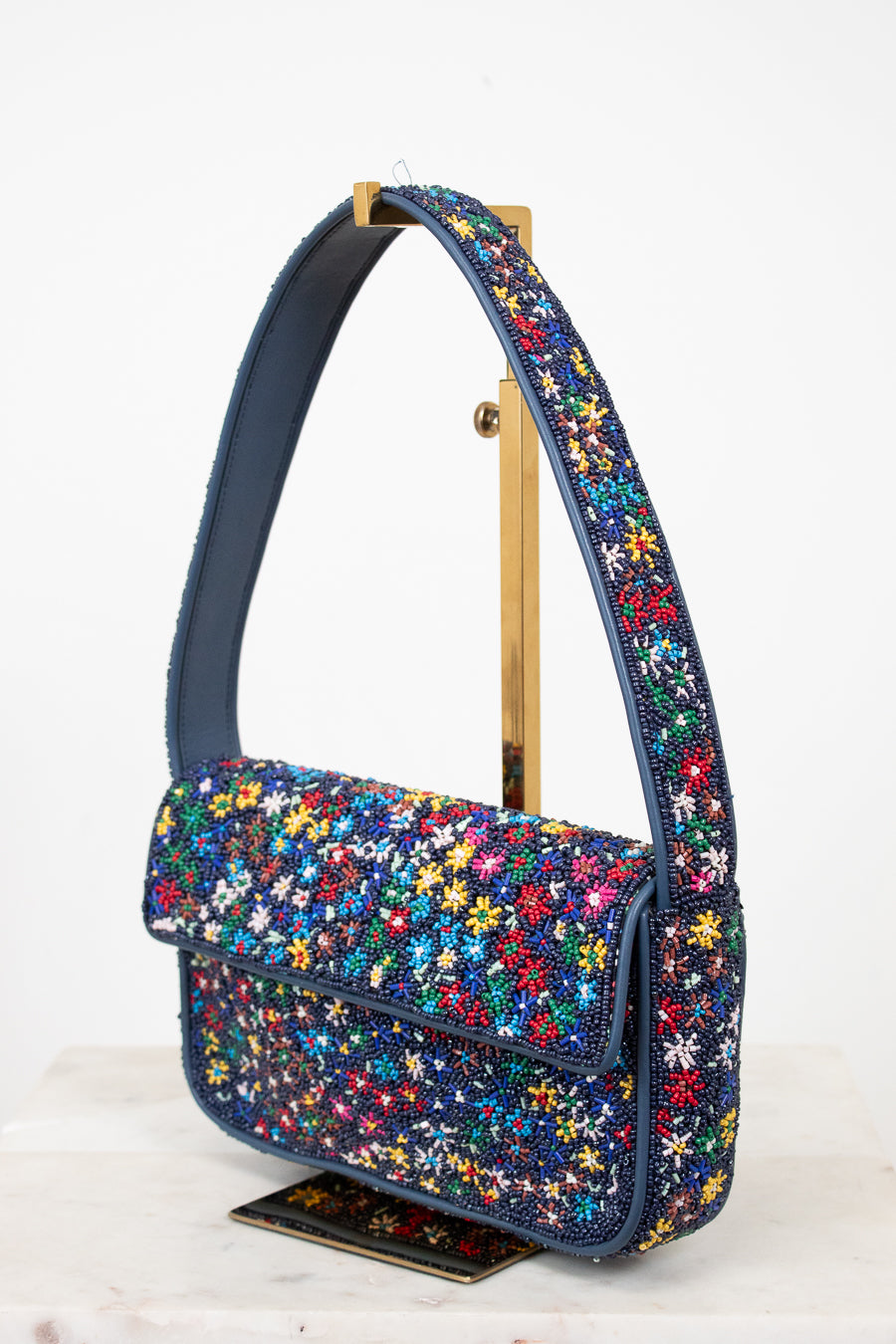 Multicolored floral patterned beaded handbag on a gold stand on a white background