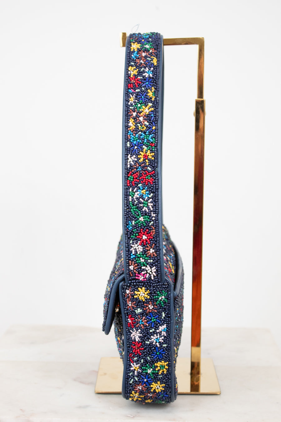 Side profile of handbag with colorful beaded floral pattern on a stand against a white background