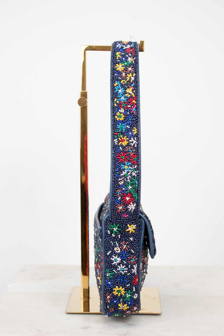 Floral-patterned side profile of beaded handbag strap on a stand against a white background