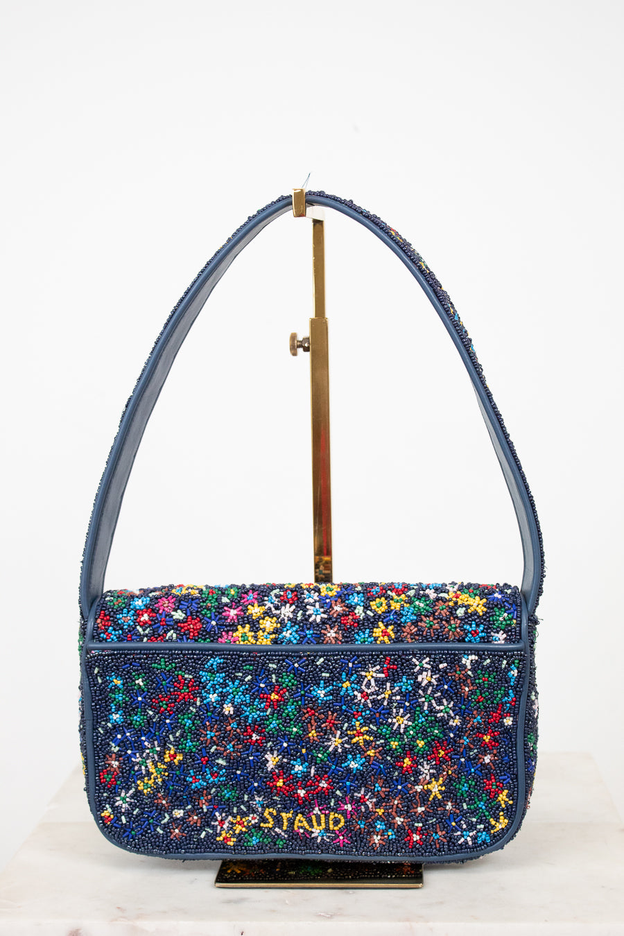 Multicolored floral-patterned handbag with 'Staud' branding on a white background