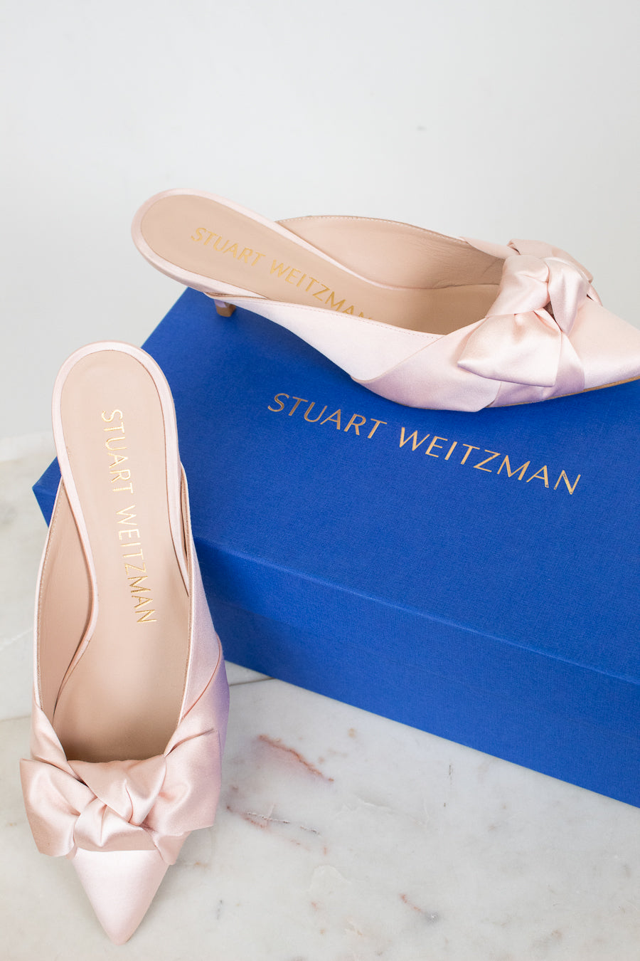 Pink satin shoes with bows on a Stuart Weitzman box