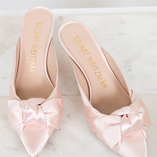 Pink kitten-heeled shoes with satin bows on a marble surface