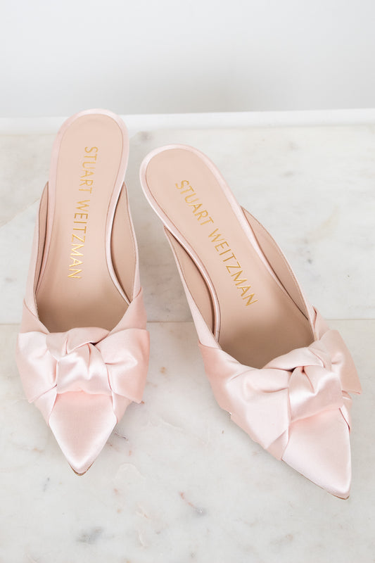 Pink kitten-heeled shoes with satin bows on a marble surface