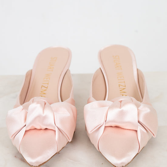 Pair of pink satin shoes with bows on a light background