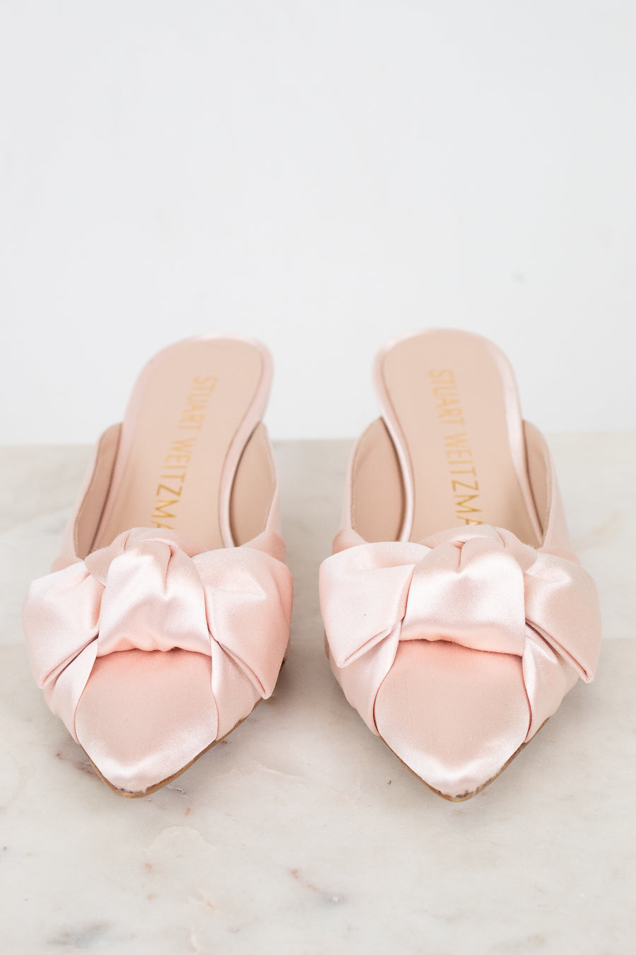 Pair of pink satin shoes with bows on a light background