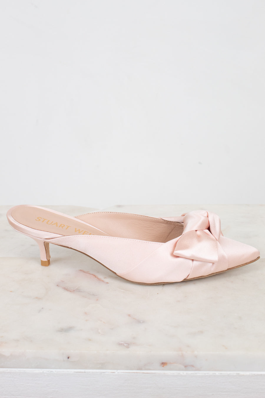 Pink kitten-heeled shoes with a bow on a marble surface