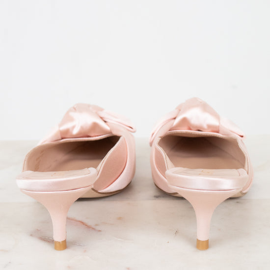 Pair of pink kitten-heeled shoes with bow details on a light background