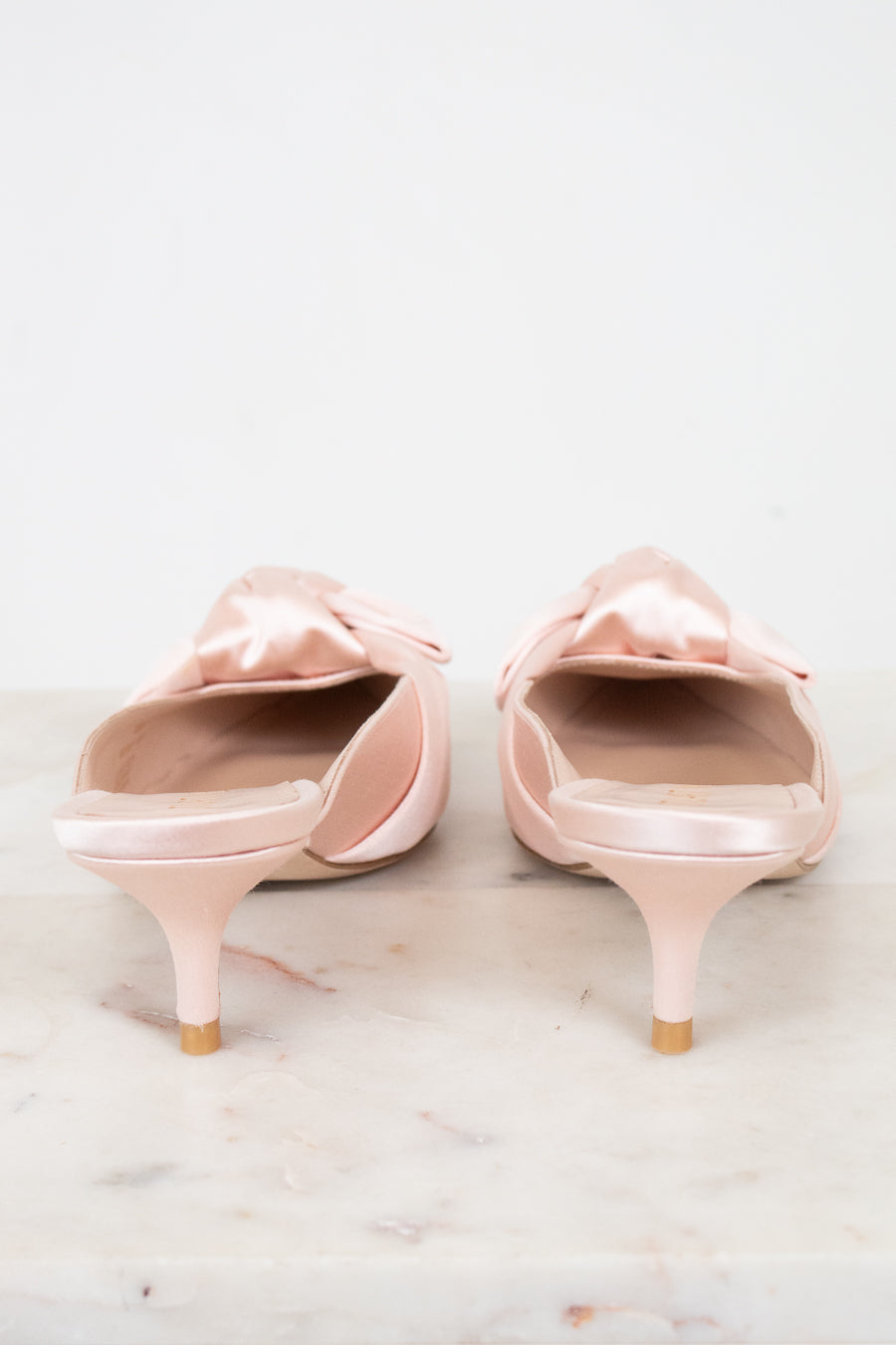 Pair of pink kitten-heeled shoes with bow details on a light background