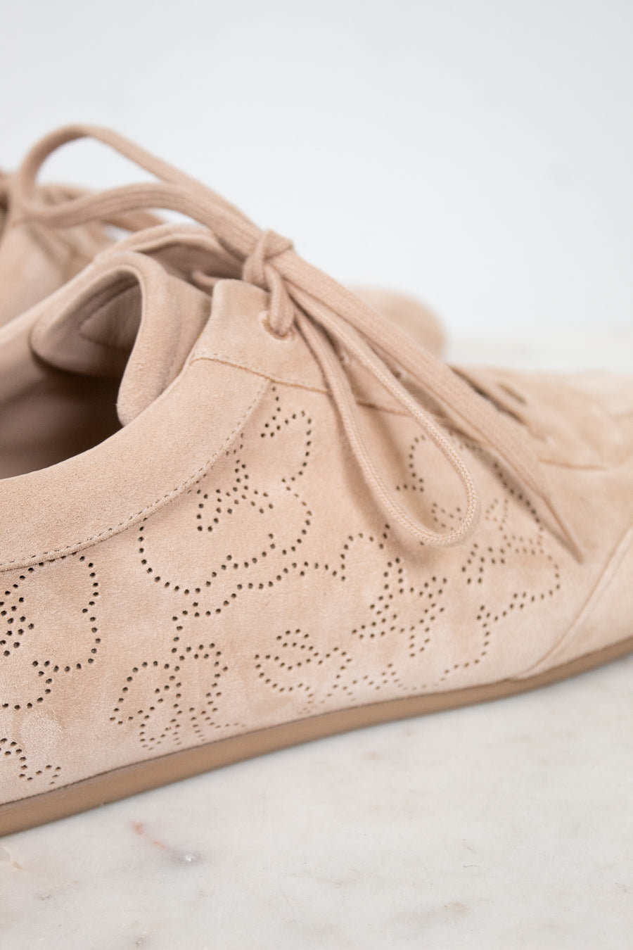 Beige suede shoe with decorative cut-out design on a light background