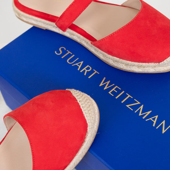 Red espadrilles on a blue box with 'Stuart Weitzman' branding.
