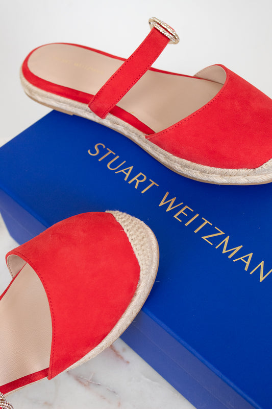 Red espadrilles on a blue box with 'Stuart Weitzman' branding.