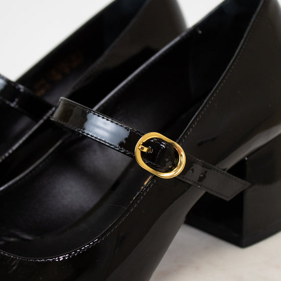 Black patent leather shoes with a gold buckle on a light background