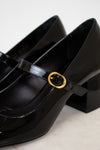Black patent leather shoes with a gold buckle on a light background