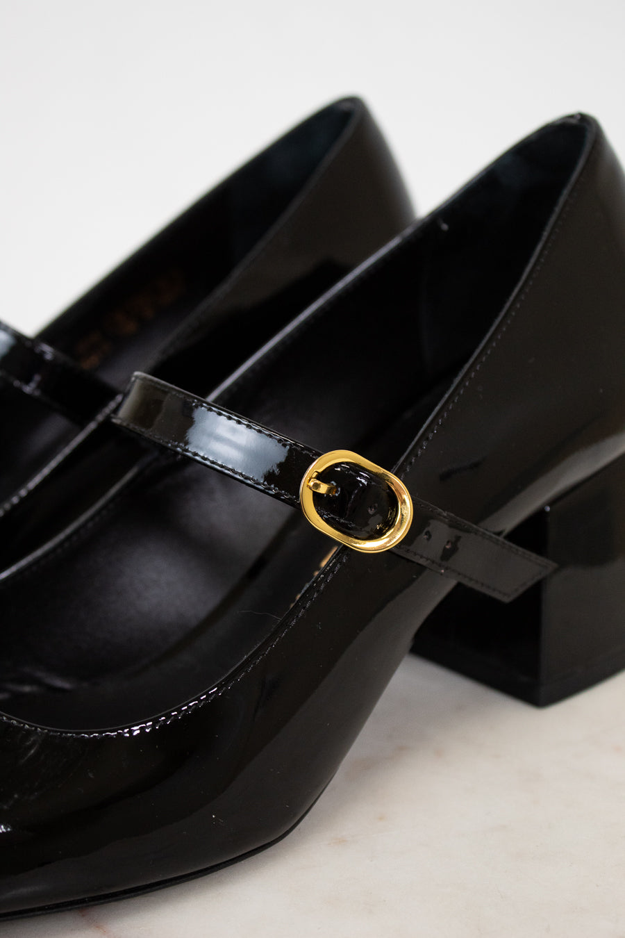 Black patent leather shoes with a gold buckle on a light background