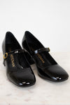 Black patent shoes with gold buckle on a light background