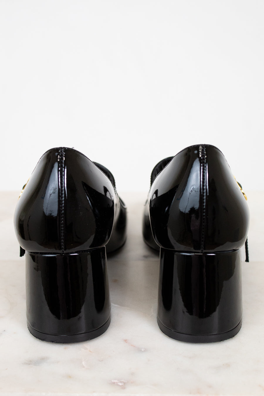 Back of black patent leather shoes on a light marble surface