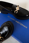 Black loafers with decorative charm on a blue Stuart Weitzman box.